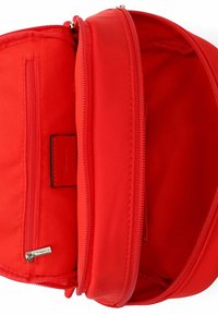 Mochila de tela roja con dos compartimentos principales. Cuenta con cremalleras y un pequeño bolsillo interior. Textura suave con detalles mínimos de herrajes.