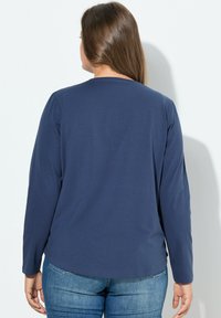 Námořnická modrá dlouhá rukávová blůza z měkkého a hladkého materiálu s kulatým výstřihem a švy, doplněná světlomodrými džíny.