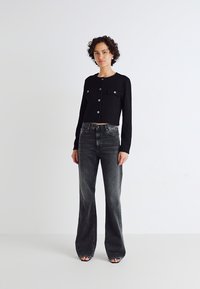 Black cropped jacket with long sleeves, buttons, and two front pockets, paired with high-waisted, faded grey flared jeans.