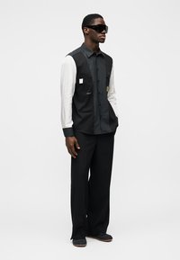 Chemise oversize noir et blanc avec manches contrastantes, dotée d'une poche avant. Pantalon noir ample et lunettes de soleil complètent le look.