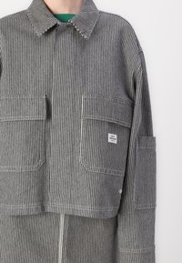 Chaqueta a rayas en blanco y negro, con un cuello, mangas largas, dos bolsillos delanteros y una etiqueta de marca en el lado derecho. Tejido texturizado.