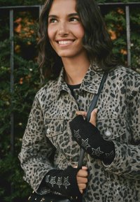 Černé bezprstové rukavice s hvězdnými ozdobami, nošené na ruce sevřené kolem popruhu. Osoba má na sobě džínsovou bundu s leopardím potiskem.