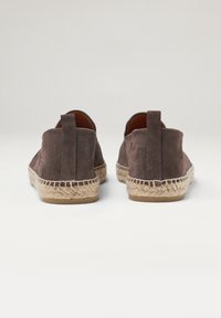 Espadrilles de ante marrón con suela tejida de yute y un talón blando y plano. Presentan una pequeña lengüeta en el talón para facilitar el calzado.
