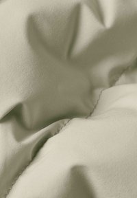 Tessuto verde chiaro con una texture liscia, caratterizzato da morbide pieghe e cuciture, indicative di un design imbottito.