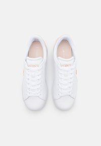 Paire de baskets blanches Lacoste avec des lacets blancs et de subtils accents beiges, vue de dessus sur un fond uni.