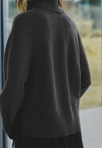 Dunkelgrauer Strickpullover mit hohem Kragen, gerippten Bündchen und einer strukturierten Gestaltung im oberen Rückenbereich. Weiches Material und lockere Passform.