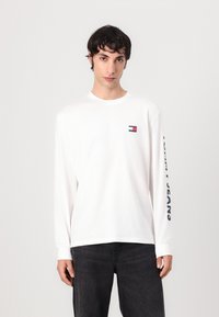 Witte lange mouwen T-shirt van katoen met een ronde hals, met een klein logo op de borst en "TOMMY JEANS" in marineblauw gedrukt op de mouw.