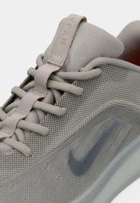 Zatvoreni kadar svijetlosivog Nike tenisica s mrežastim gornjim dijelom, podstavljenim jezikom, zaobljenim vezicama i tamnosivim swoosh logom na strani.