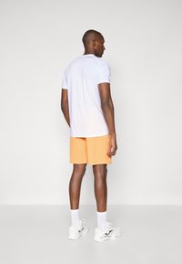 White short-sleeve shirt with a smooth texture, paired with orange shorts. The outfit is completed with white athletic shoes and socks.