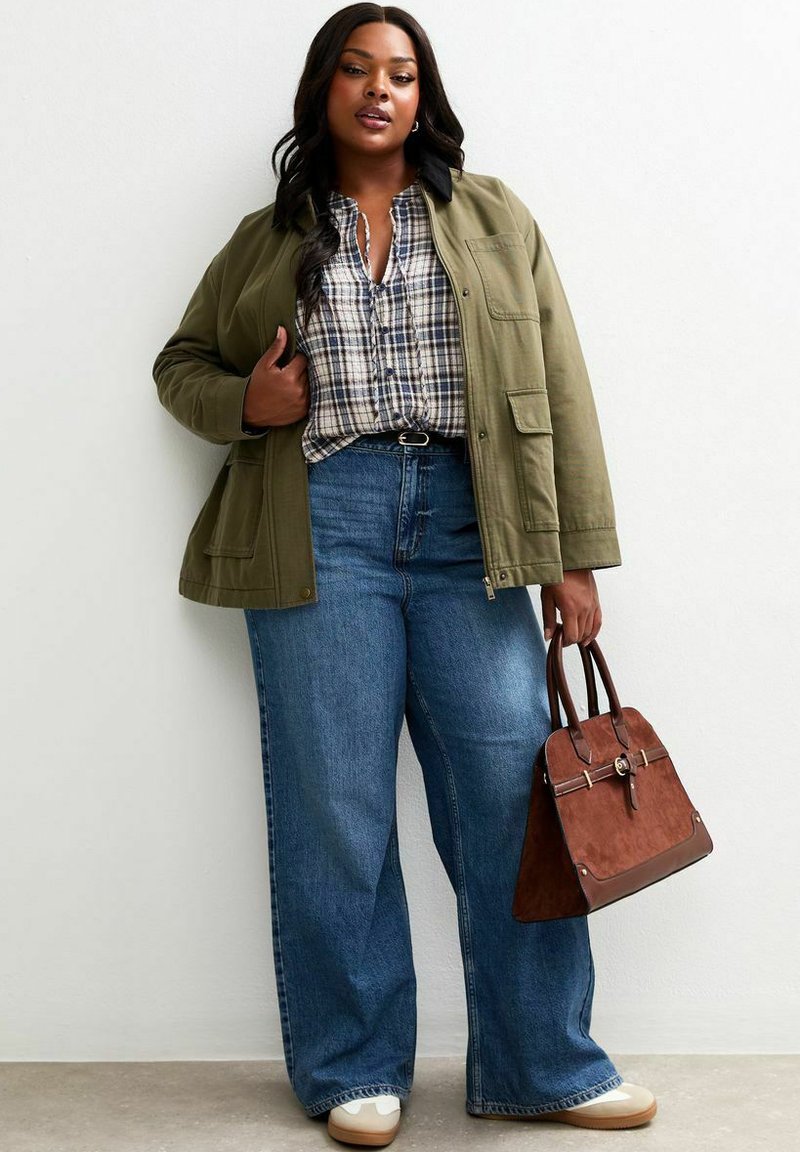 Olivgrön jacka, rutig skjorta, vida blå jeans och brun handväska. Vita sneakers med texturerad sula fulländar outfitten.