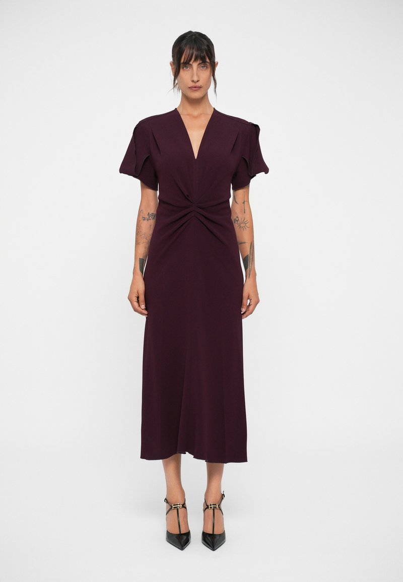 Burgundy dress with a deep V-neck, knotted front detail, and flutter sleeves. Its midi length and smooth texture complement pointed black heels.