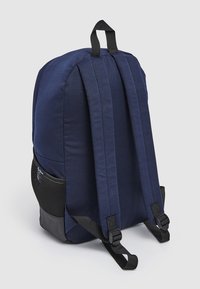 Mochila de tela azul marino con correas de hombro acolchadas, un asa superior y un bolsillo de malla lateral. Presenta una base negra y una textura duradera.