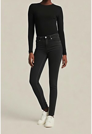 Person wearing fitted black long-sleeve top, high-waisted black skinny jeans, and white sneakers standing against a plain background.