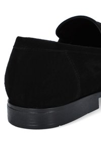 Czarne zamszowe buty wsuwane z zaokrąglonym tyłem, teksturowaną powierzchnią i niską, żłobioną gumową podeszwą. Brak widocznych elementów metalowych czy akcentów.