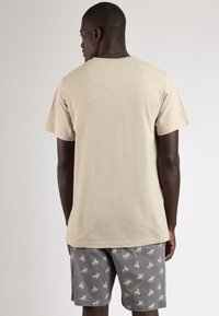 Camiseta de manga corta beige con un corte relajado, combinada con pantalones cortos grises que presentan un patrón repetitivo de animales en color claro.