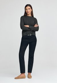 Pull en maille torsadée gris foncé, pantalon noir et mocassins en suède beige. Design ajusté avec des poignets côtelés et un col rond.