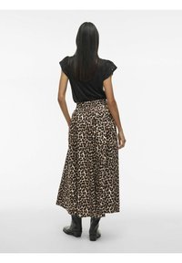 Top nero a maniche corte con dettagli arricciati abbinato a una lunga gonna beige con stampa leopardata marrone e stivali neri alla caviglia.