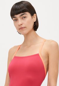 Fuchsia tank topp med tynne, lyse oransje stropper. Glatt tekstur, minimalistisk design og firkantet utringning.