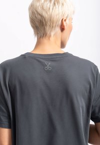 Grijze t-shirt met korte mouwen van zachte katoen, met een subtiele schaarmotief geborduurd op de achterkant. Glad textuur en een ontspannen pasvorm.