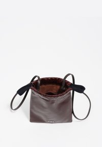 Mała ciemno-brązowa skórzana torba na sznurek z czarnymi paskami, otwarte dno ukazujące miękką podszewkę wewnętrzną oraz małe srebrne logo marki z przodu.