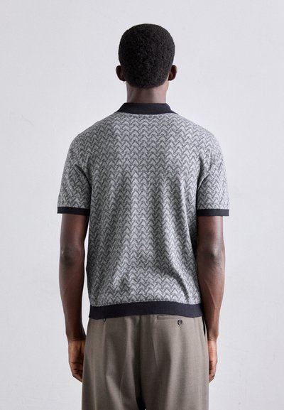 Polo tricot gris à manches courtes avec un motif chevron, col et poignets noirs, associé à un pantalon beige. Texture lisse, coupe décontractée.