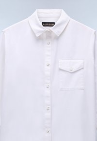 Camicia bianca button-up con colletto classico e taschino singolo sul petto. Realizzata in tessuto liscio con una finitura leggermente testurizzata.