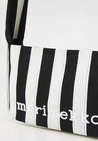 Borsa in tessuto a righe bianche e nere con texture a coste, dotata di tracolla e logo "marimekko" ricamato sul fronte.