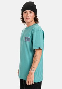 Tyrkysové bavlněné tričko s krátkými rukávy, s grafickým potiskem v růžové a černé na hrudi a malým logem na rukávu.