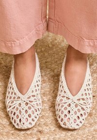 Bailarinas blancas tejidas con un diseño abierto, con punta afilada y un pequeño lazo decorativo. Textura suave y material blando.