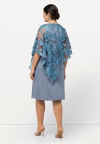 En blå klänning med en genomskinlig, broderad spetsjal som har blommönster. Kjolen är knälång och har en rak silhuett.