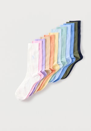 Naskladané pastelovo farebné rebrované ponožky v bielej, ružovej, levanduľovej, béžovej, oranžovej, žltej, mätovej, svetlomodrej, modrej, olivovej a námorníckej modrej na bielom pozadí.