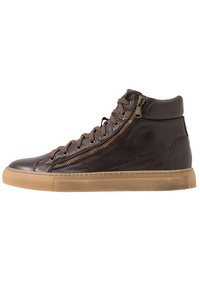Sneaker montante en cuir marron avec fermeture éclair sur le côté, bout rond et semelle en caoutchouc à texture légère. Les lacets ajoutent un détail de fermeture supplémentaire.