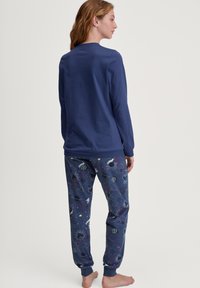 Marineblauw longsleeve T-shirt met een ronde hals, gecombineerd met joggerbroeken met een patroon van hemelse ontwerpen in verschillende kleuren. Zachte stof.