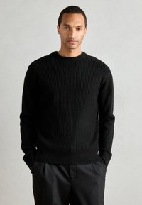 Pulover negru din tricot cu striații, cu gât rotund și mâneci lungi, având un model texturat și un tiv ajustat. Purtați peste pantaloni negri.