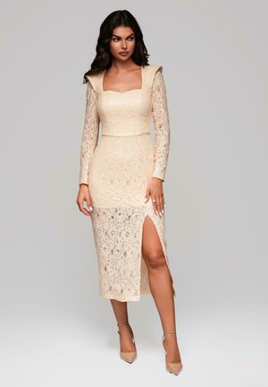 Lace midi-klänning i ljusbeige med långa ärmar, fyrkantig halsringning och sid slits. Har delikata blommönster och figurnära silhuett.