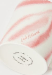 Keramični kozarec z belo osnovo in rožnatimi vijugastimi vzorci. Na spodnji strani označen z napisom "Café Kitsuné" in podatki o izdelku.