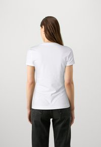 Camiseta blanca de algodón ajustada con cuello redondo, mangas cortas y textura suave, vista desde la parte de atrás. Jeans negros de cintura alta.