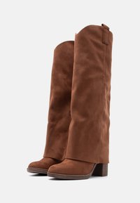 Καφέ μπότες σουέντ μέχρι το γόνατο με υφή, με τακούνια block και στρογγυλεμένη μύτη. Διαθέτουν διακριτική ραφή και θηλιά στο πάνω μέρος.
