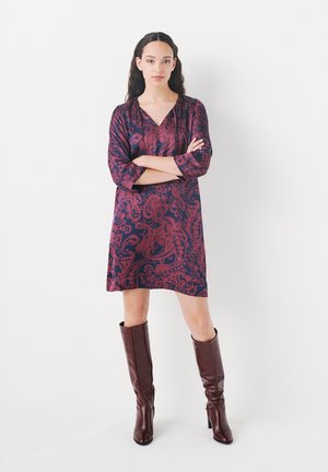 Abito a fantasia in blu navy e bordeaux con scollo a V e maniche a trequarti, abbinato a stivali in pelle marroni fino al ginocchio.