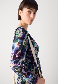 Robe à manches longues présentant un motif floral dans des teintes de violet, vert et bleu sur une base claire. Tissu texturé avec un corsage ajusté et une jupe fluide.