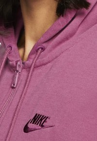 Paarse zip-up hoodie met een zachte textuur, voorzien van een klein zwart Nike-logo op de borst en trekkoorden op de capuchon.
