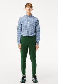 Chemise à carreaux bleus avec col, assortie à un pantalon slim vert et des baskets noires avec des accents verts.