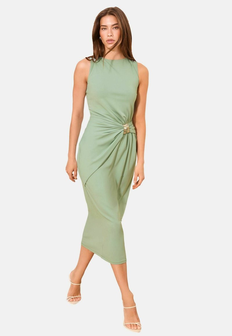 Woman wearing a sleeveless light green midi dress with a side knot detail and strappy beige high-heeled sandals walking forward.
