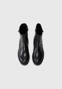 Botas de tobillo de cuero negro con un acabado suave, puntera redonda, cierre de cremallera lateral y detalles de panel texturizado en la parte superior.
