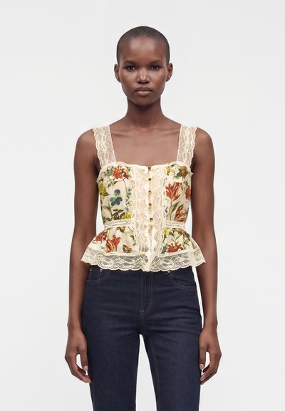 Mannequin mince portant un corset à dentelle florale avec des boutons et un jean taille haute foncé sur un fond clair uni.