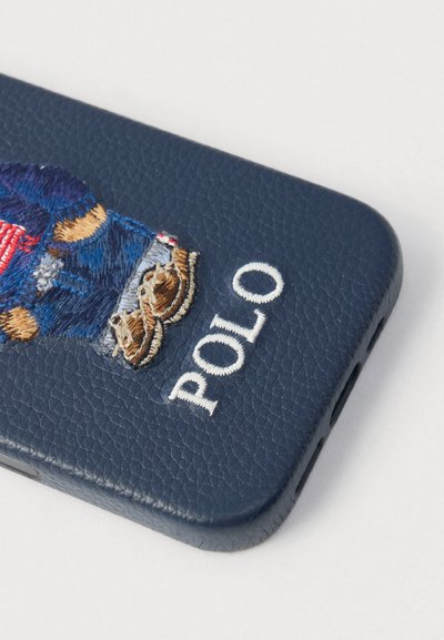 Θήκη τηλεφώνου από δέρμα ναυτικού μπλε χρώματος με κεντητό σχέδιο αρκούδας σε μπλε και κόκκινο, με την επιγραφή "POLO" σε λευκά γράμματα. Επιφάνεια με υφή.