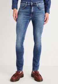 Jeans de mezclilla azul con un diseño ajustado, que presentan un lavado claro, un leve desgastado, cinco bolsillos y costuras en contraste. Acabados con un botón de metal.
