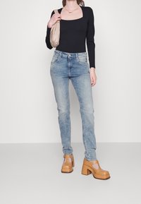 Top negro de manga larga con escote cuadrado, vaqueros azul claro y tacones de plataforma marrones con detalles recortados. Sosteniendo un bolso beige.