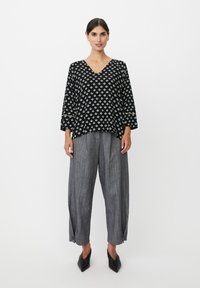 Zwart topje met patroon, v-hals en driekwart mouwen, gecombineerd met grijs gestreepte wijde pijpen broek en zwarte puntige platte schoenen.