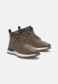 Hnědé kožené kotníkové boty s texturovaným povrchem, hnědé tkaničky, polstrovaný límec a bílé gumové podrážky s akcentem z gumy.